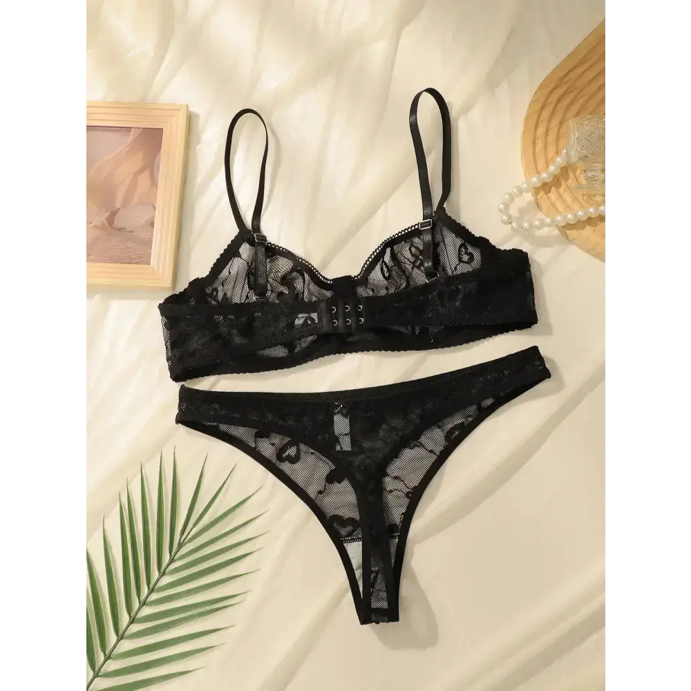 Black sexy lace lingerie set featuring sheer bra and matching thong on cream fabric background