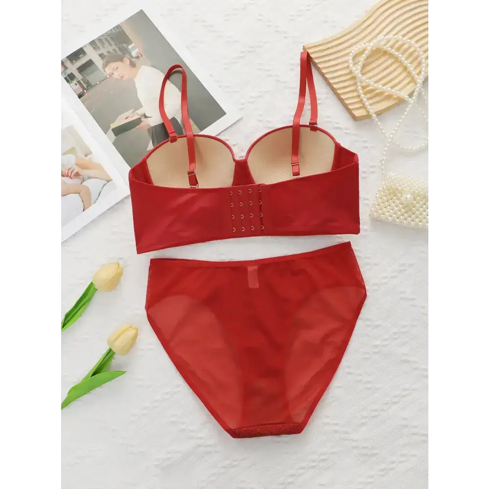 Sexy red bra and panty set from The Lady's Haven Boutique laid flat with decorative flowers and accessories