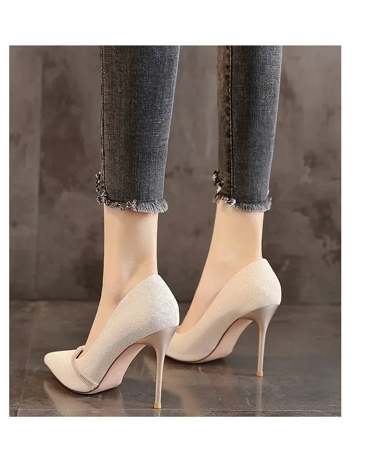 Elegant beige single strap stiletto heels worn with frayed ankle jeans on a dark floor