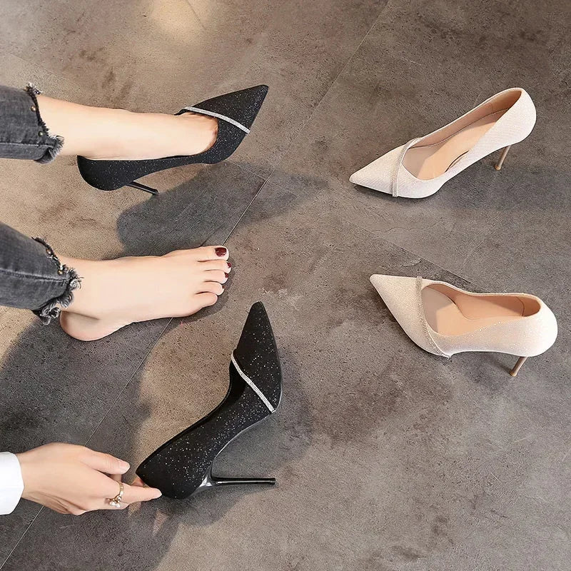 Black and white single strap stiletto heels displayed on a gray floor with a person wearing one black heel