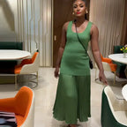 Woman wearing sleeveless green maxi dress standing in a modern dining area with colorful chairs