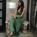 Woman wearing sleeveless green maxi dress sitting on stone bench with decorative sheep legs
