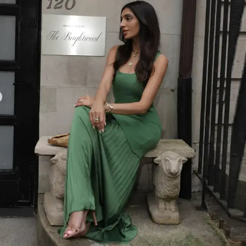Woman wearing sleeveless green maxi dress sitting on stone bench with decorative sheep legs