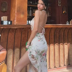 Woman wearing sleeveless tie back floral dress with high slit standing at wooden bar