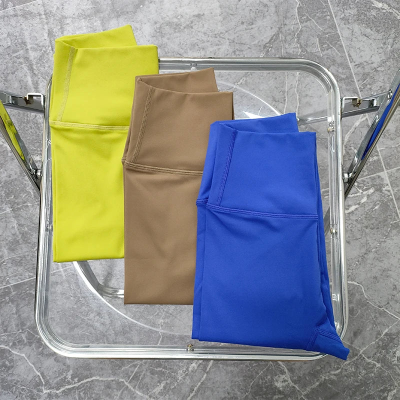 Stylish two piece workout clothing for women featuring bright yellow, tan, and blue leggings folded on a chair