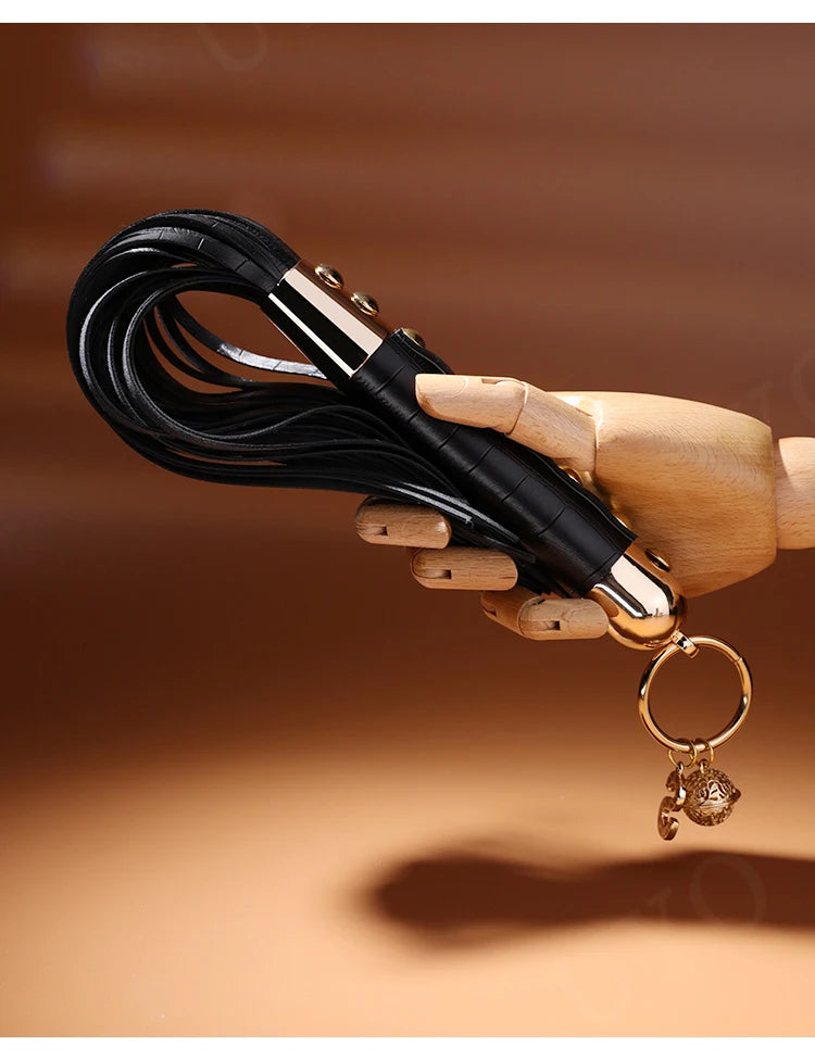 Couple punishment BDSM whip black leather flogger with gold handle and charms held by wooden mannequin hand