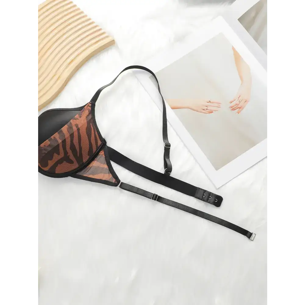 Fashion leopard bra and underwear set with black straps laid on white surface beside artwork and woven mat
