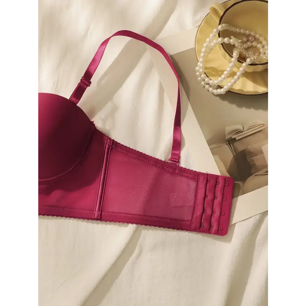 Wine red lingerie set bra with adjustable straps and hook closure laid on white fabric next to pearl necklace