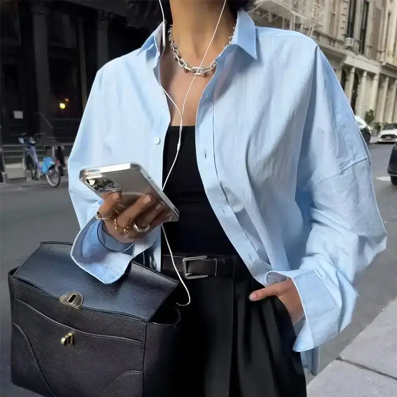 Light blue spring long sleeve office shirt worn over black top with black pants and black handbag