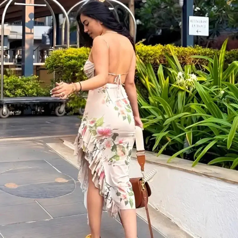 Woman wearing sleeveless tie back floral dress with ruffle hem carrying brown handbag outdoors