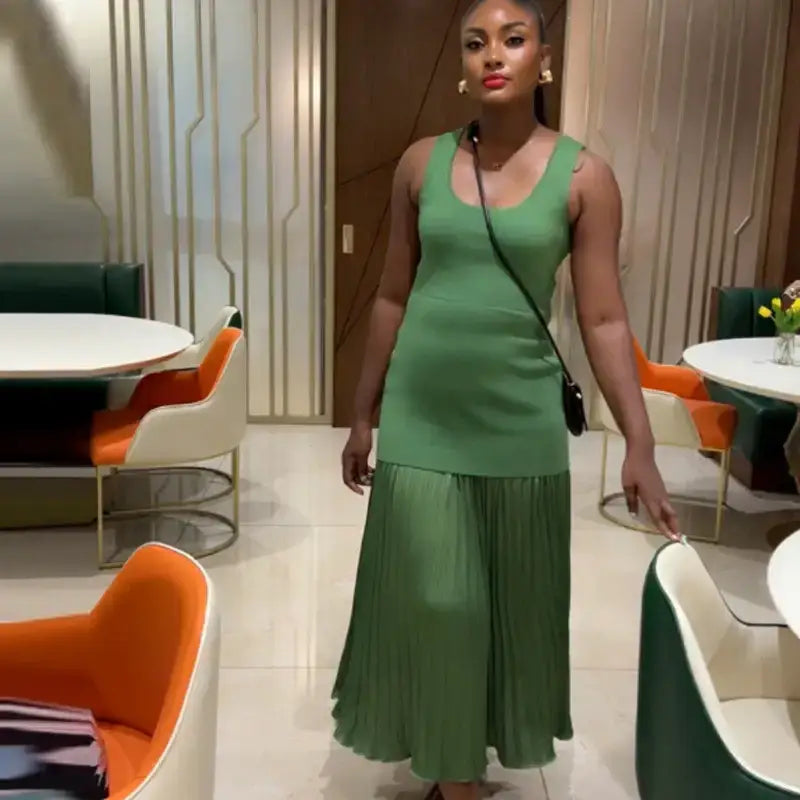 Woman wearing sleeveless green maxi dress standing in a modern dining area with colorful chairs