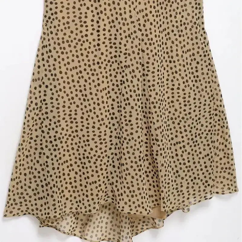 Close-up of beige elegant polka dot maxi dress with black spots and flowing fabric