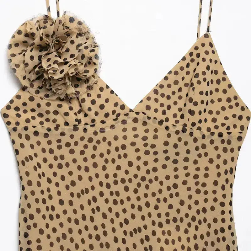 Close-up of elegant polka dot maxi dress with beige fabric and black dots featuring a floral embellishment