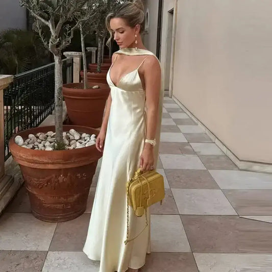 Elegant sleeveless satin formal dress in light champagne worn by woman holding yellow handbag outdoors