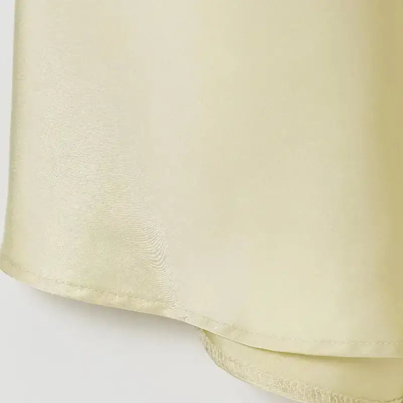 Close-up of pale yellow sleeveless satin formal dress fabric hem with smooth texture from The Lady's Haven Boutique