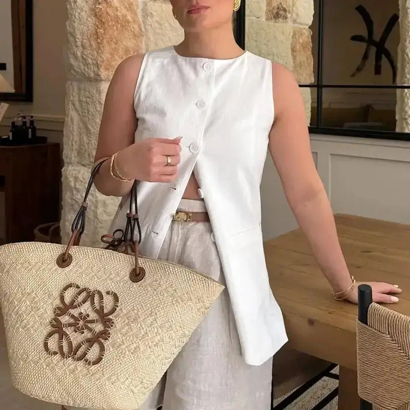 Woman wearing a white sleeveless summer office vest and shorts outfit holding a large woven tote bag indoors